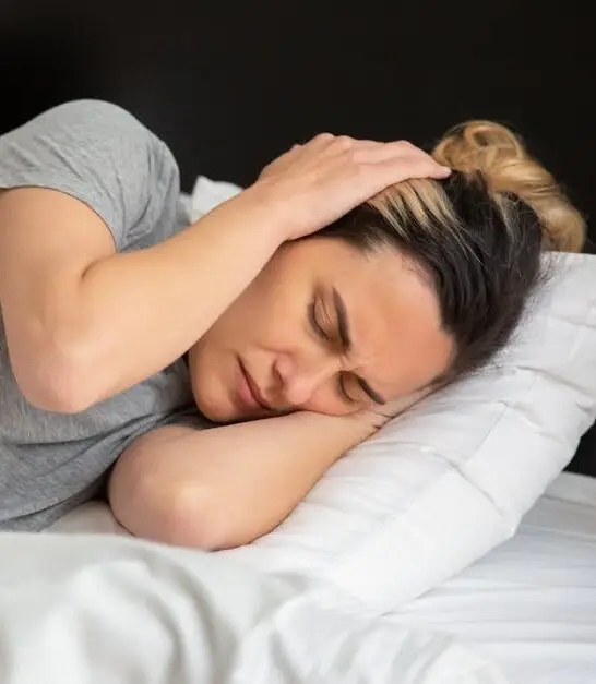 A woman looks frustrated in bed as her partner snores loudly, highlighting sleep disturbance issues.